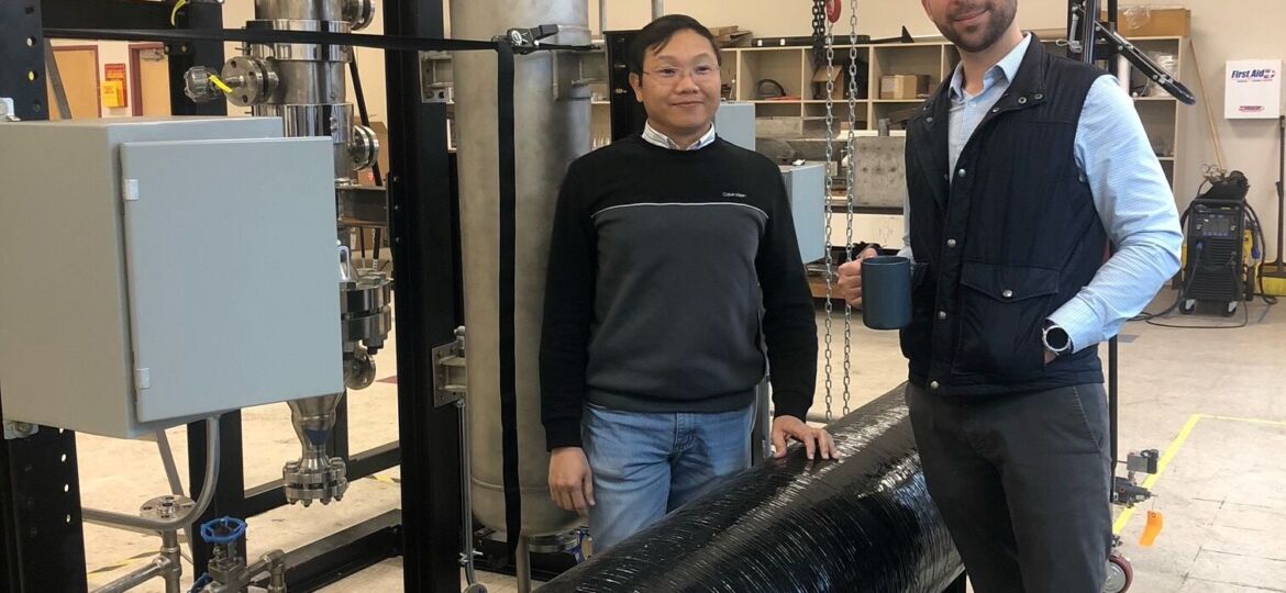 2 men standing in front of hydrogen reactor system